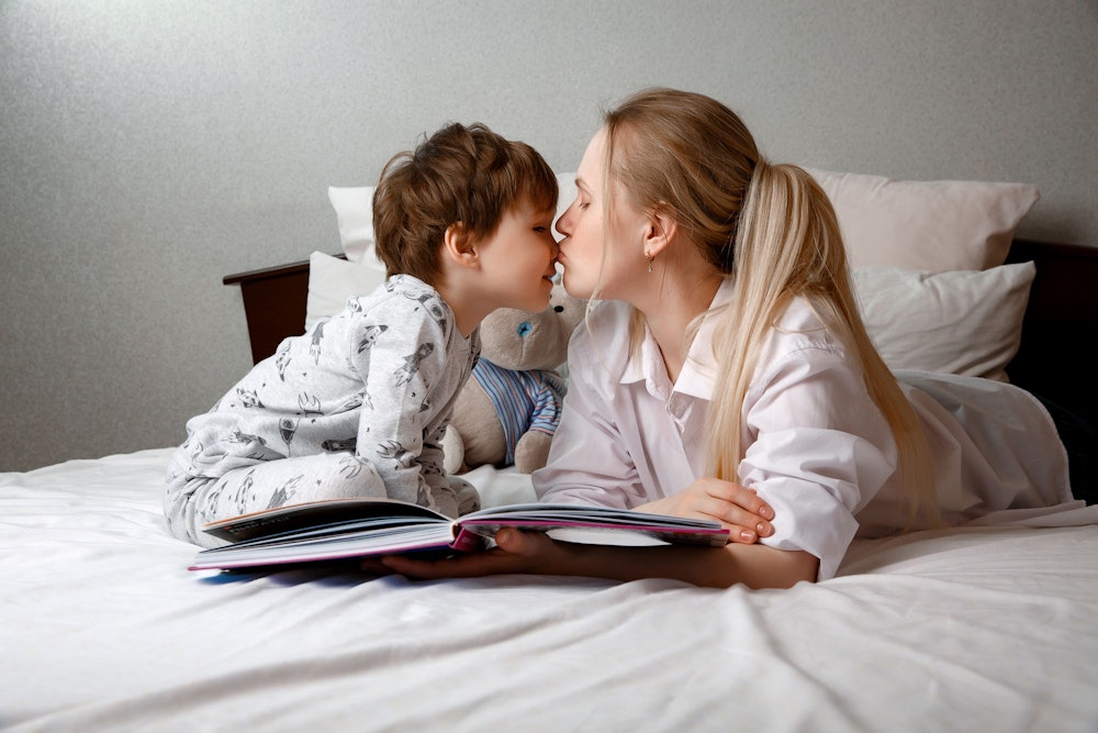 Mother kissing child's nose while reading