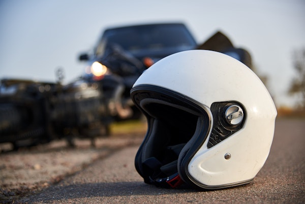 Close up of motorcycle helmet on the road with a fallen motorcycle and car in the background