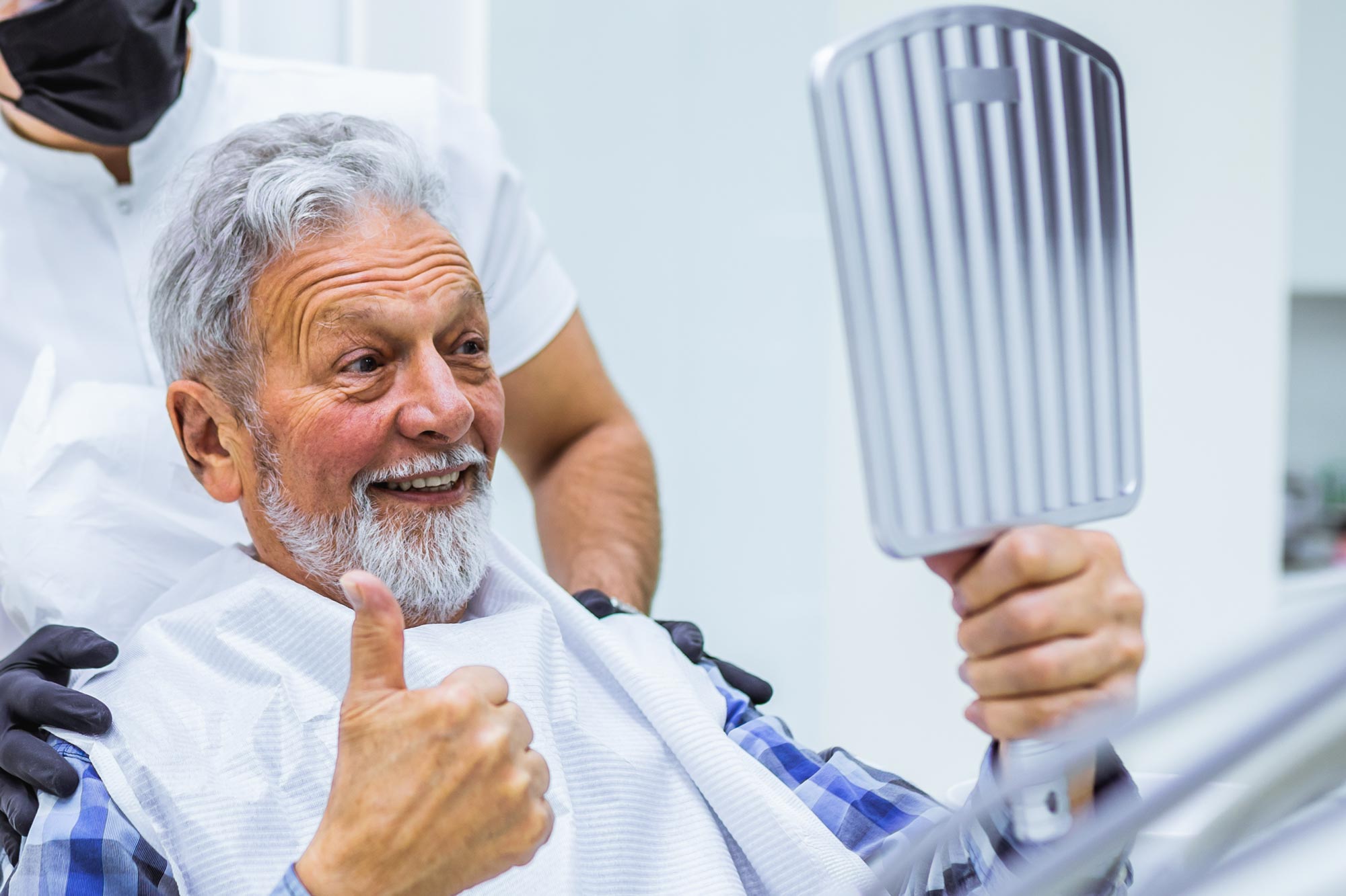 man in a dentist chair looking in a mirror and smiling while holding a thumbs up