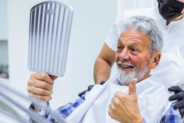 Smiling mature man giving a thumbs up in the mirror at the dentist office