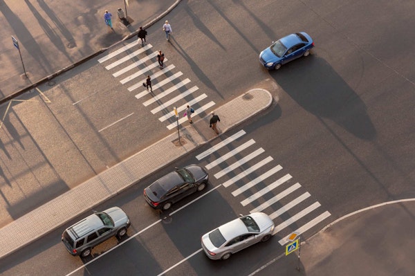 Pedestrians crossing crosswalk with cars waiting and driving