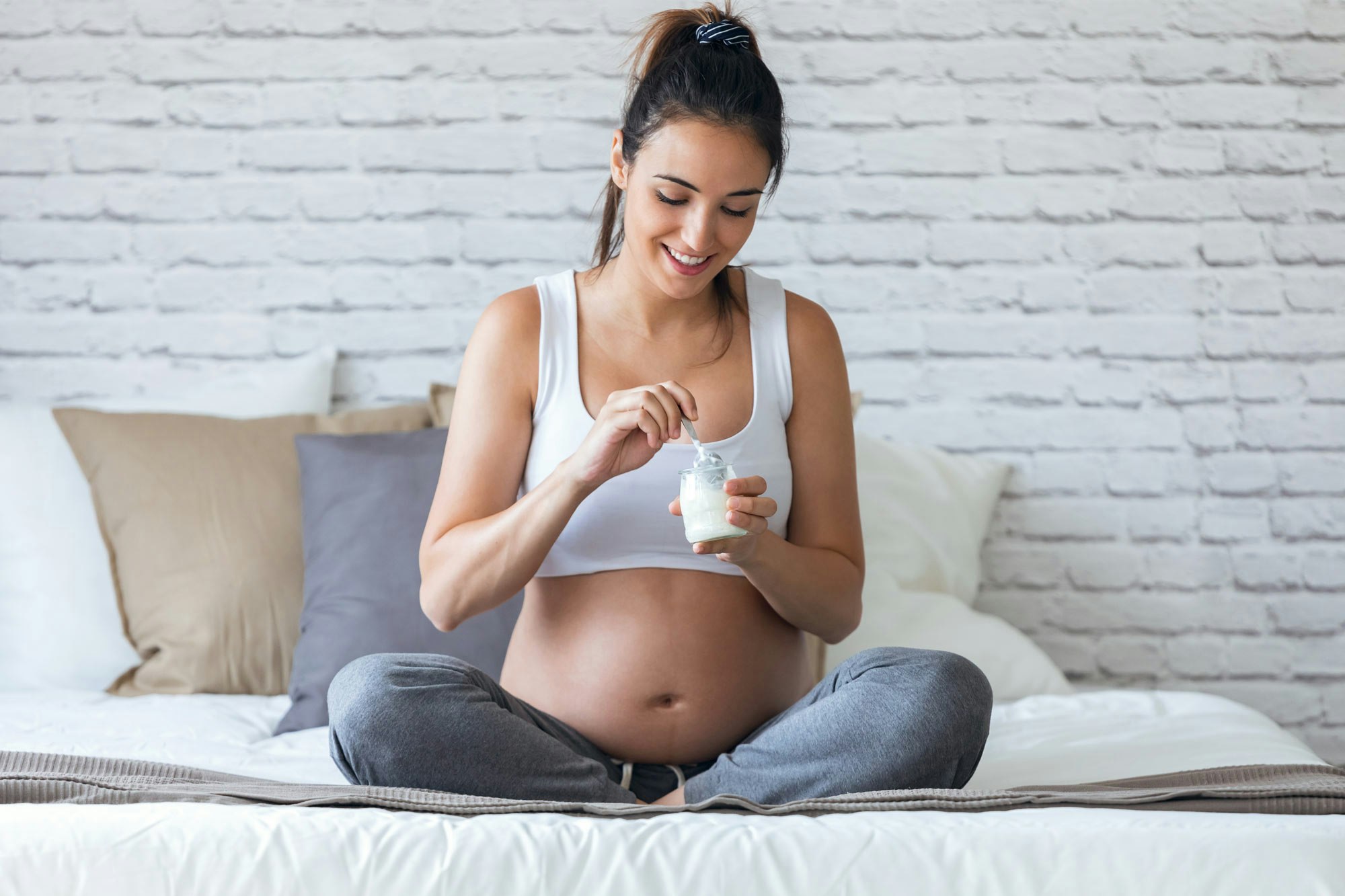 Pregnant woman eating yogurt on bed