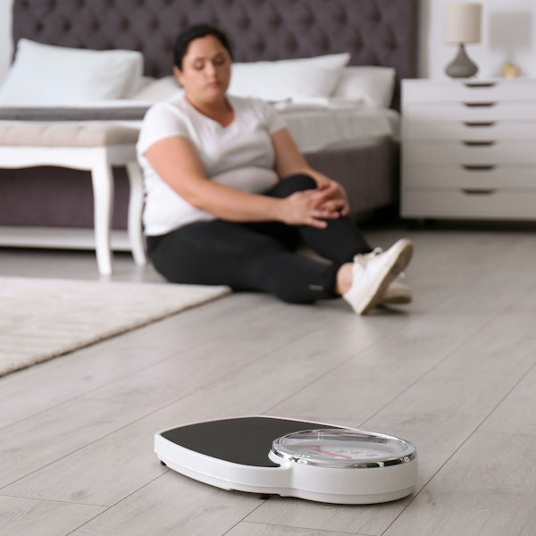 sad woman in the background looking at a weight scale