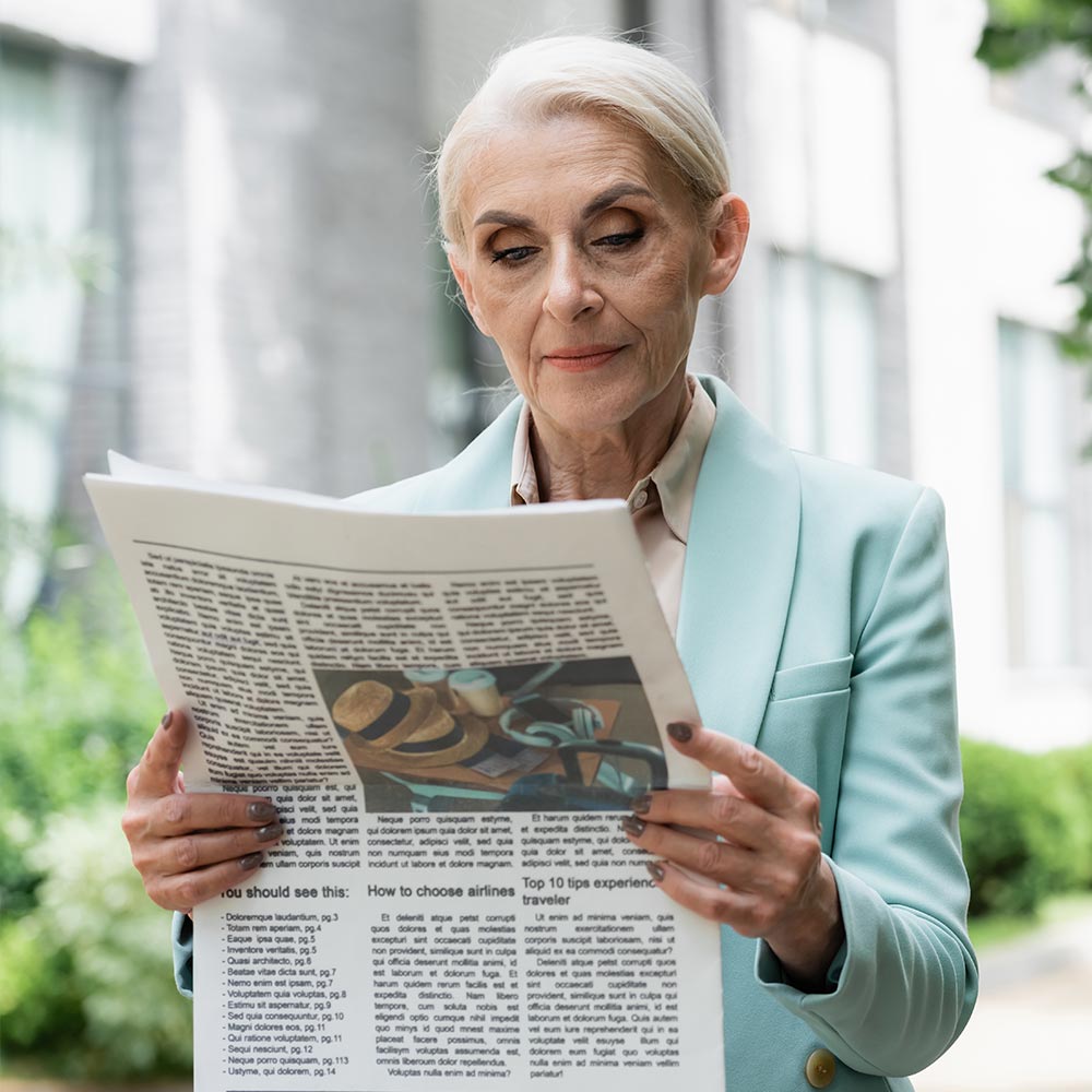 Mature woman trying to read newspaper outdoors
