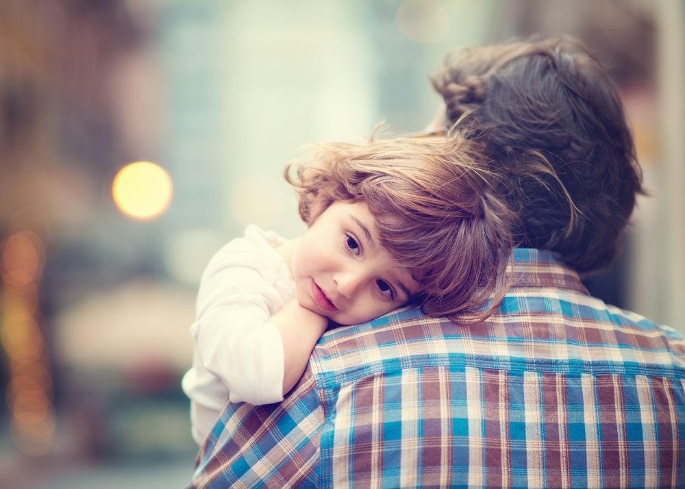 young child resting head on parent’s shoulder