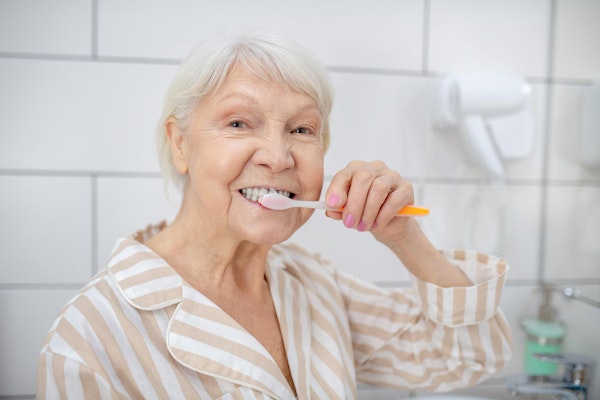Mature woman with dental implants brushing teeth