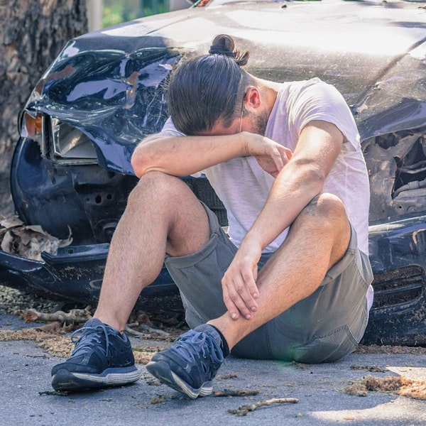 Man sitting in front of smashed car from hit-and-run