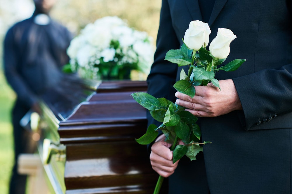 Man holding roses in front of a casket