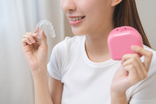 Smiling teenage girl holding a clear aligner and carrying case