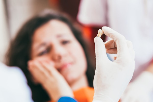 Tooth in gloved hand with patient in background with hand on jaw