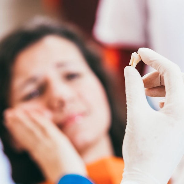 Tooth in gloved hand with patient in background with hand on jaw