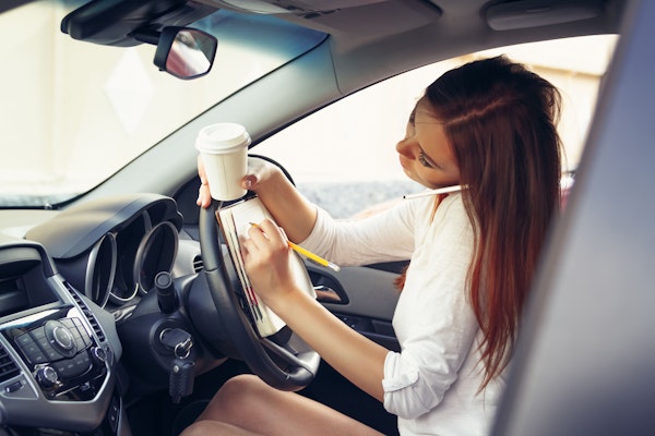 Woman distracted by coffee cup and notebook while driving