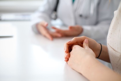A doctor and patients hands, sitting on a table folded while they have a conversation