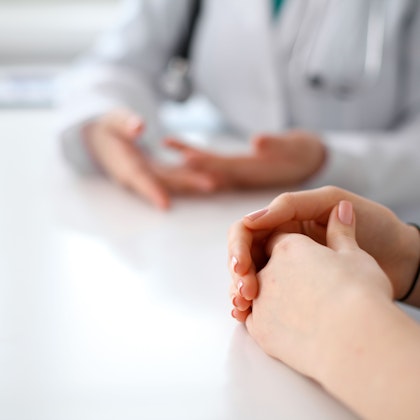 A doctor and patients hands, sitting on a table folded while they have a conversation