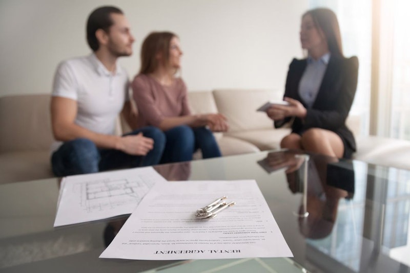 A rental agreement on a desk, and a couple on a couch speaking with a real estate lawyer.