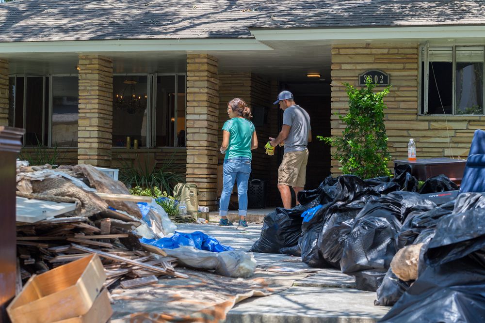 man and woman standing outside their home with trash bags and damaged property on the yard