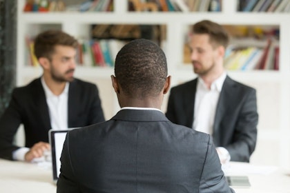 Black office worker sits across table from two white office workers