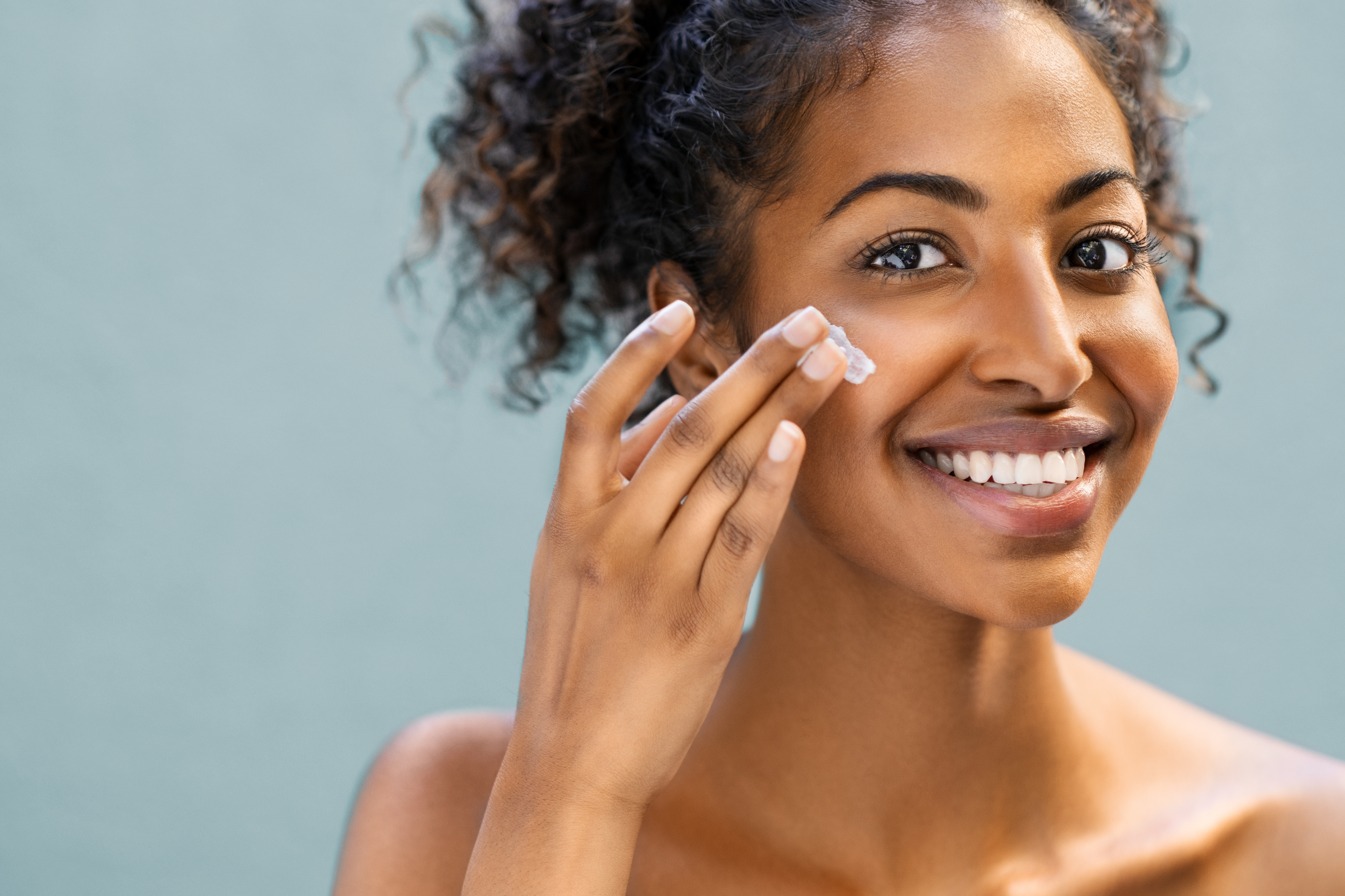 Woman adding cream to her cheek while smiling