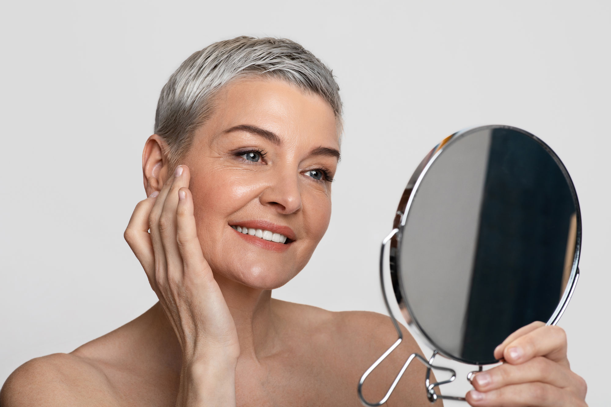 Mature woman admiring facial cosmetic surgery in mirror