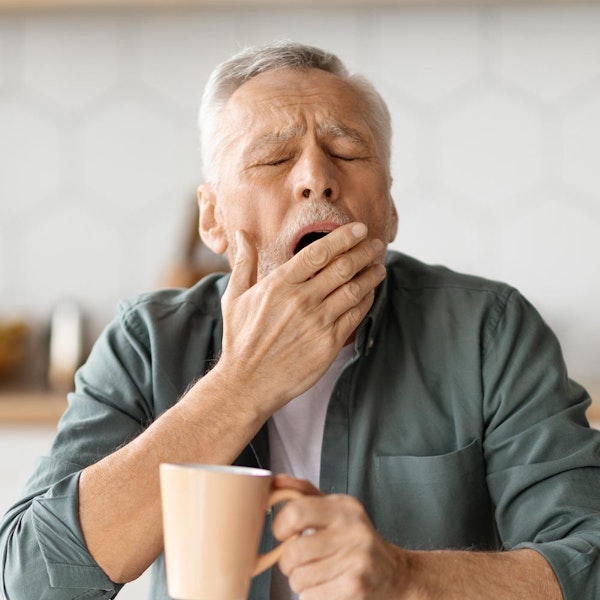 Mature man yawning while holding a mug