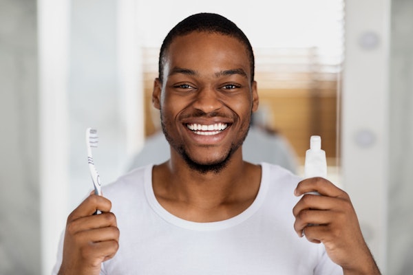 smiling man holding toothbrush and toothpaste after gum disease therapy