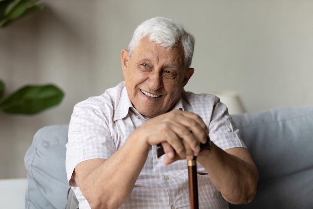 Smiling elderly man after full mouth reconstruction holding onto cane