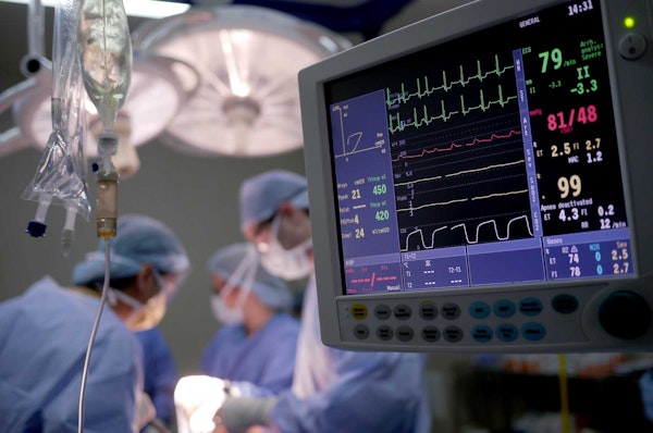 Close-up of hospital monitoring system with doctors in operating room in background