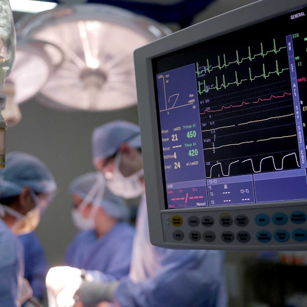 Close-up of hospital monitoring system with doctors in operating room in background