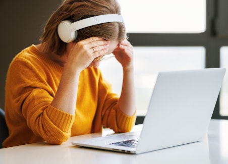 Tired young girl wearing headphones touching head