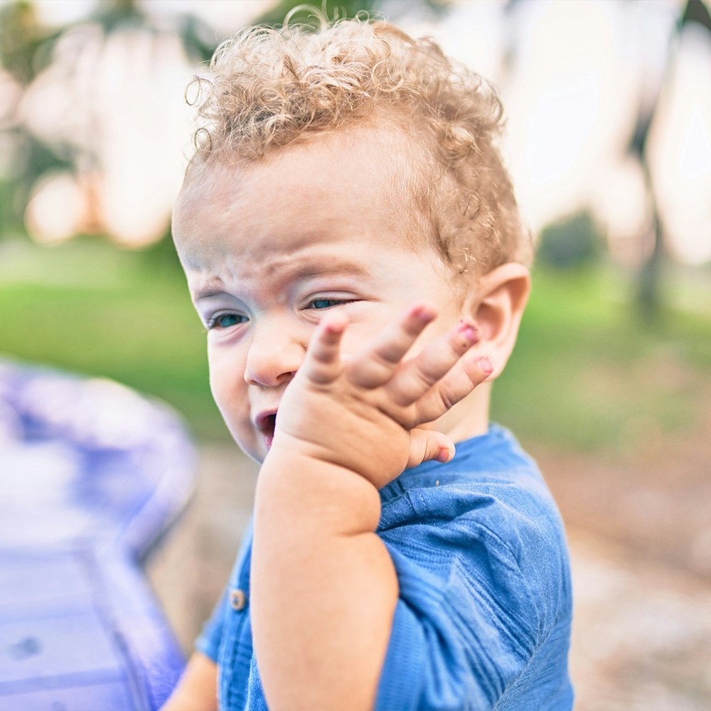 Toddler crying and holding hand to face
