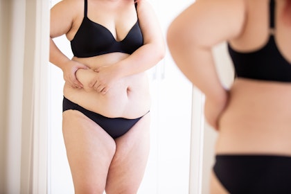 Woman holding excess fat around abdomen section while looking in the mirror