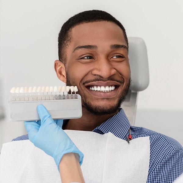 Dentist holding up veneer selection to dental patient