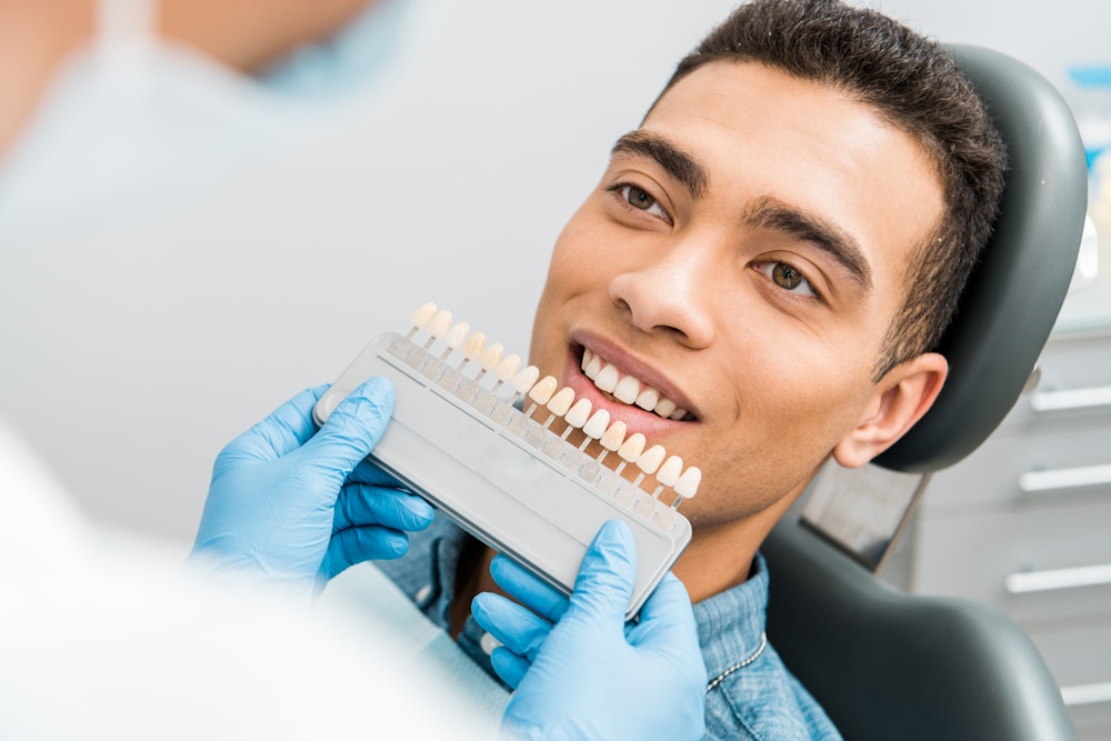 Close-up of patient's mouth comparing natural teeth to porcelain veneers before cosmetic dentistry procedure
