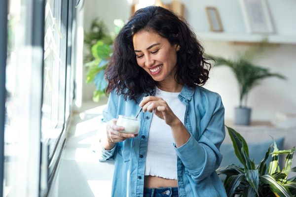 Smiling woman after tooth extraction recovering and eating yogurt at home